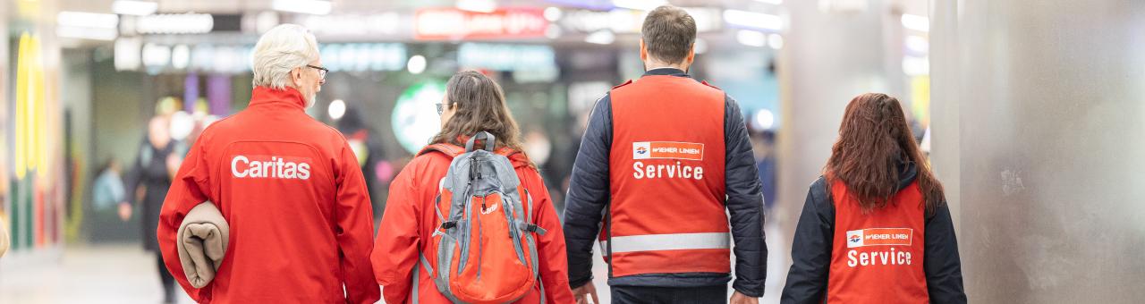 Mehrere Personen mit roten Jacken tragen Winterdecken in einer Ubahnstation